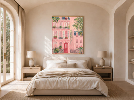 Impasto pink Parisian building wall art in a gold frame above a bed with warm linen bedding and a rattan lamp in a bright minimal bedroom with arched windows