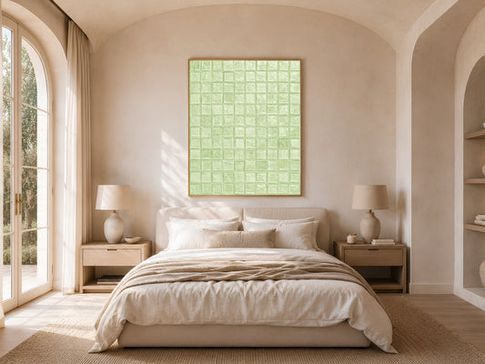 Sage green mosaic tile wall art in a gold frame hanging above a bed with warm linen bedding in a bright minimal bedroom with arched windows and a rattan lamp