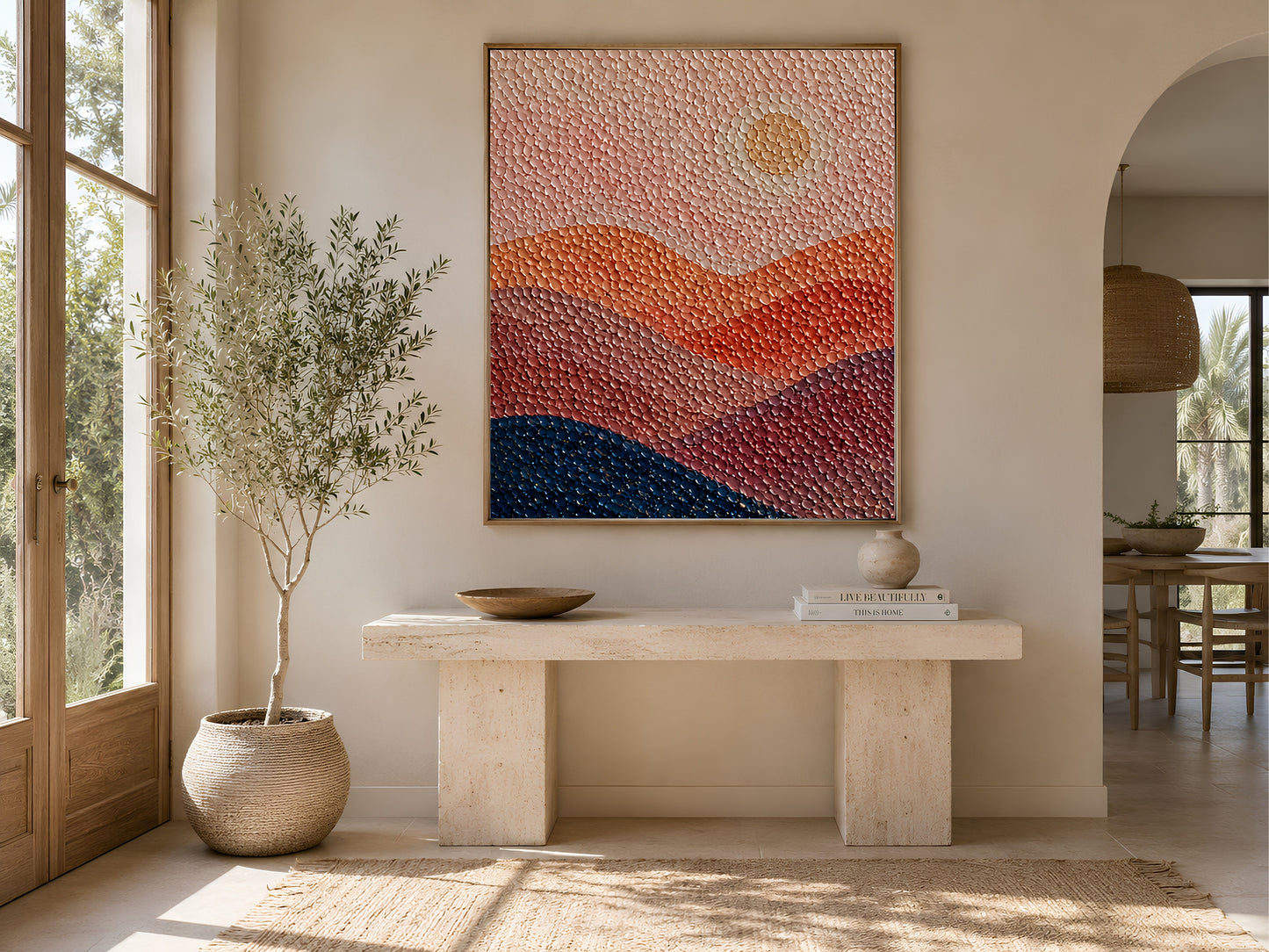 Abstract pointillist sunset print in a wooden frame displayed in a bright entryway with arched doorway, olive tree, and travertine console table