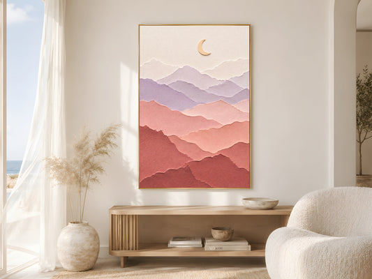 Pastel layered paper art mountain print in a gold frame beside sheer white curtains in a bright coastal living room with a round boucle chair