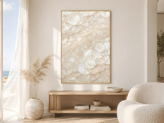 Capiz shell spiral swirl print in gold frame beside sheer curtains in bright coastal living room with cream bouclé chair and dried pampas grass