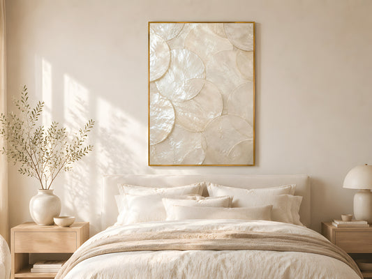 Large capiz shell abstract print in gold frame above linen bed with cream bedding in warm minimalist coastal bedroom with natural wood furniture