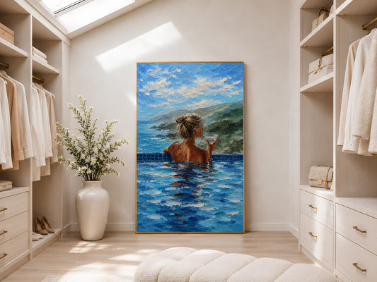 Gold-framed infinity pool woman and ocean view impasto print in a bright walk-in wardrobe with neutral shelving, recessed lighting, and a tall potted plant