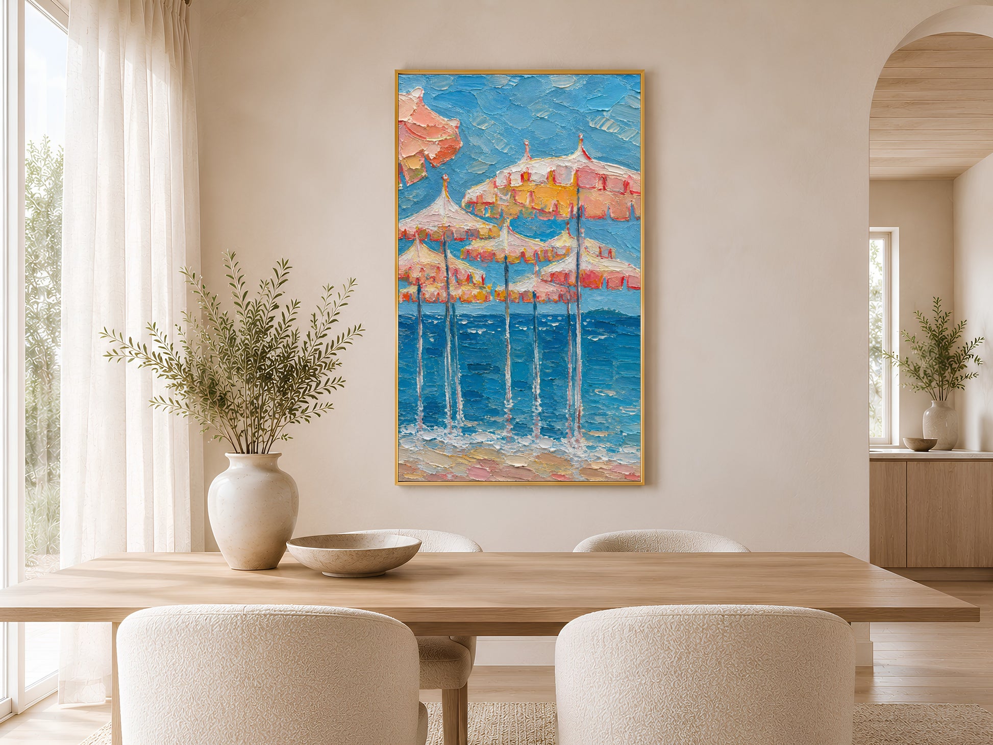 Pink beach umbrella impasto print in a gold frame on a white wall in a bright coastal living room with a round vase and dried stems
