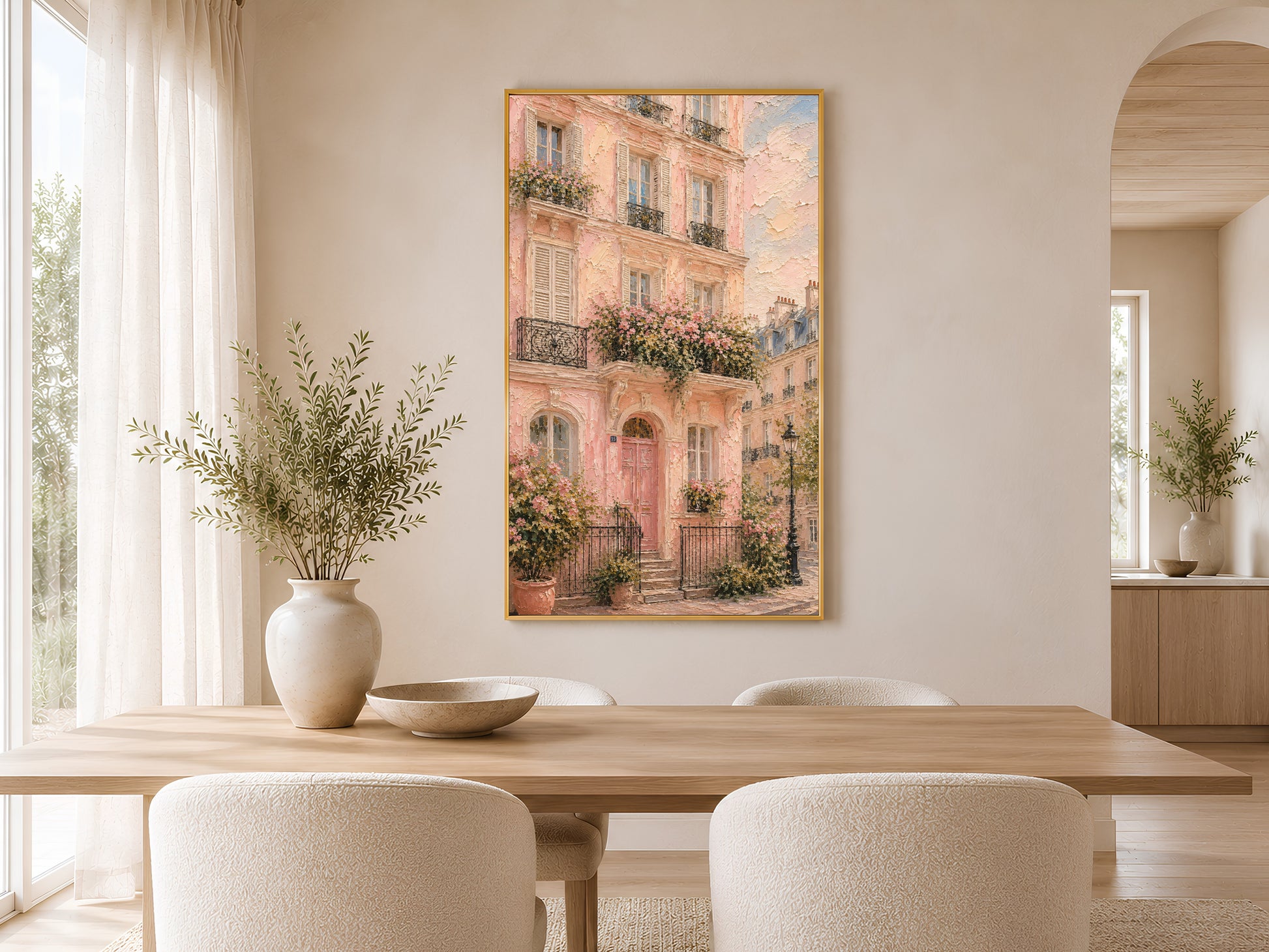 Framed pink Parisian building wall art in a warm minimal dining room with round wooden table, chairs, ceramic vases and soft natural light
