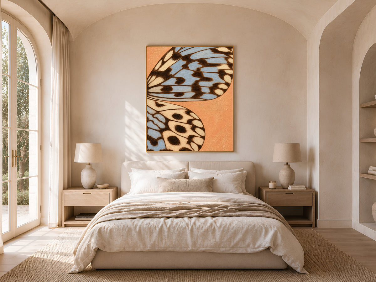 Framed terracotta blue butterfly wing art hung above a bed in a bright, airy bedroom