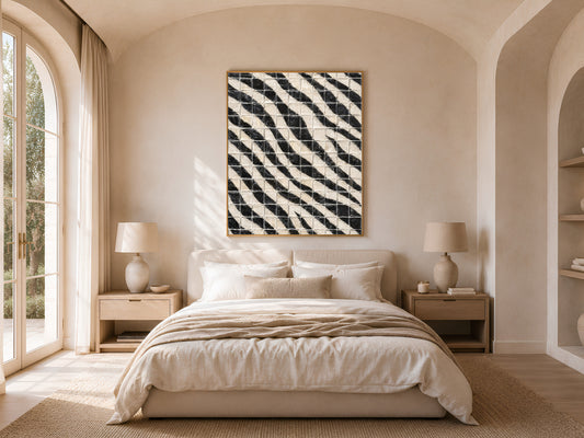Black and white diagonal stripe mosaic tile wall art in a gold frame above a bed with warm linen bedding and rattan lamps in a bright minimal bedroom with arched windows
