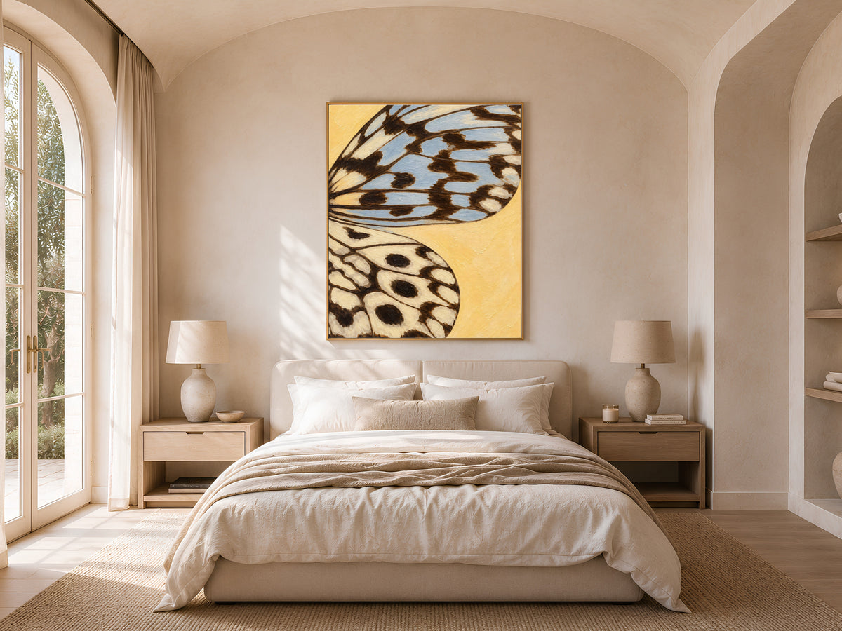 Framed butter yellow dusty blue butterfly wing art hung above a bed in a bright, arched bedroom