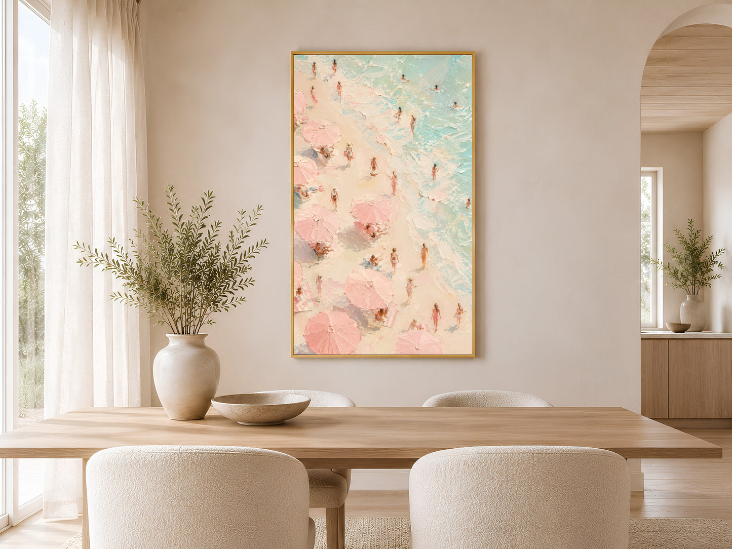 Aerial pink beach scene art in gold frame above a round dining table in a warm neutral Scandinavian dining room