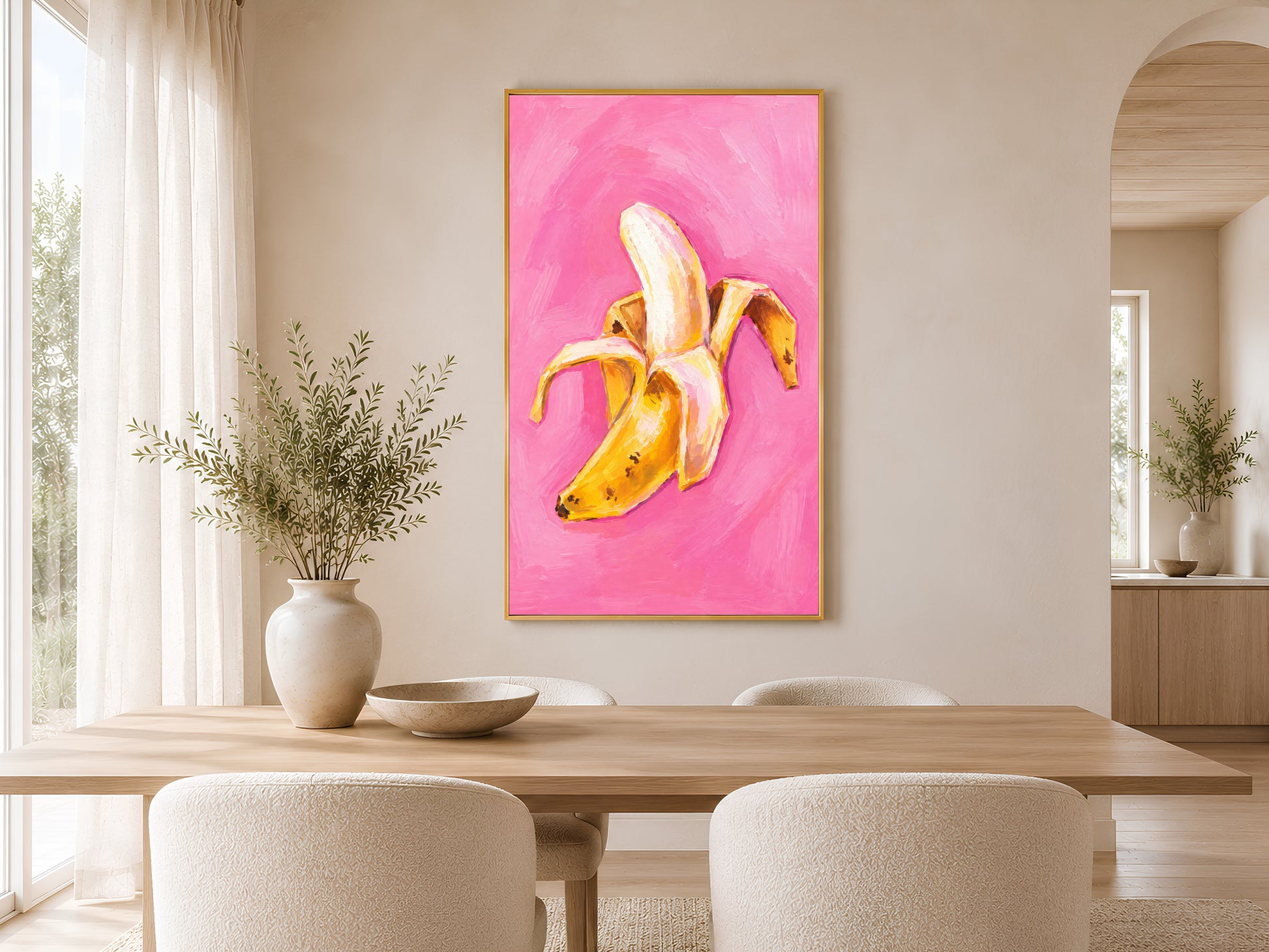 Framed impasto peeled banana print on warm beige wall above dining table with neutral chairs in minimal dining room
