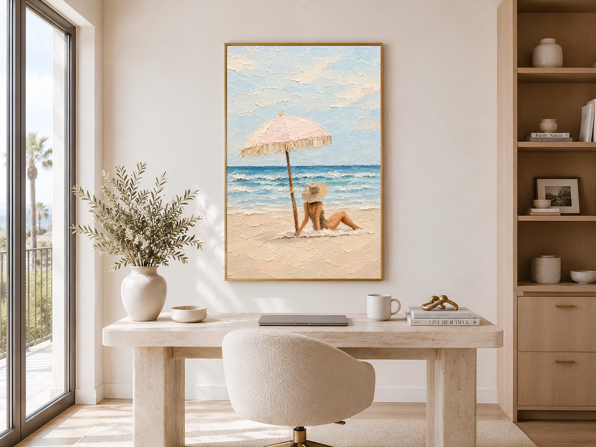 Framed beach scene wall art displayed on wall above a console table in a bright coastal room with olive tree and arched window
