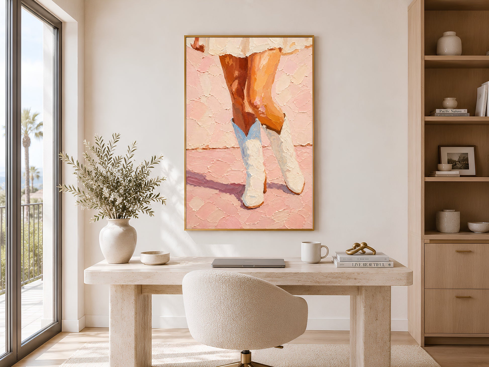 Framed pink cowgirl boots wall art displayed above a wooden vanity desk in a bright neutral home office or dressing room with soft natural light
