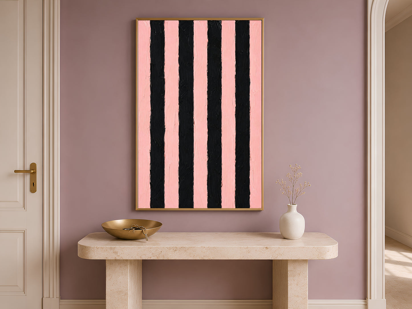 Bold pink and black stripe wall art in gold frame on travertine console table in hallway with white vase
