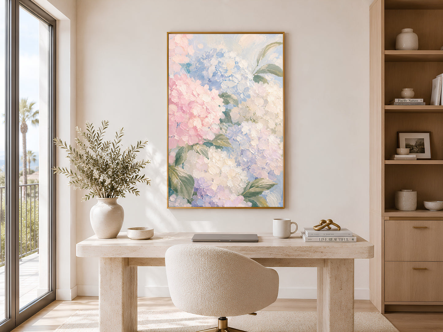 Pastel hydrangea floral print in gold frame above a round desk in a calm neutral home office with tall window