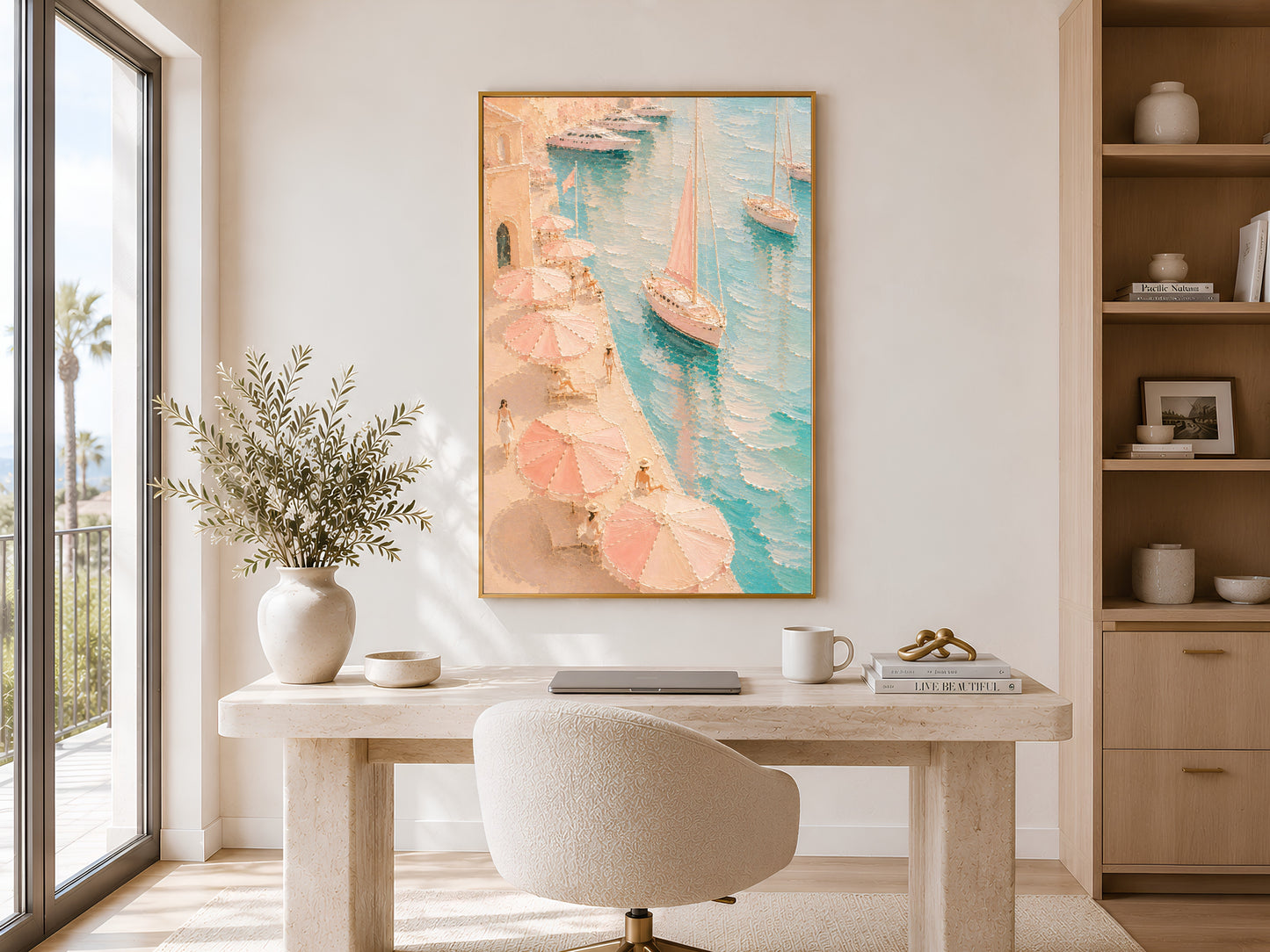 Framed Mediterranean harbor painting print in peach and teal tones in a bright home office with wooden desk, open shelving and large window
