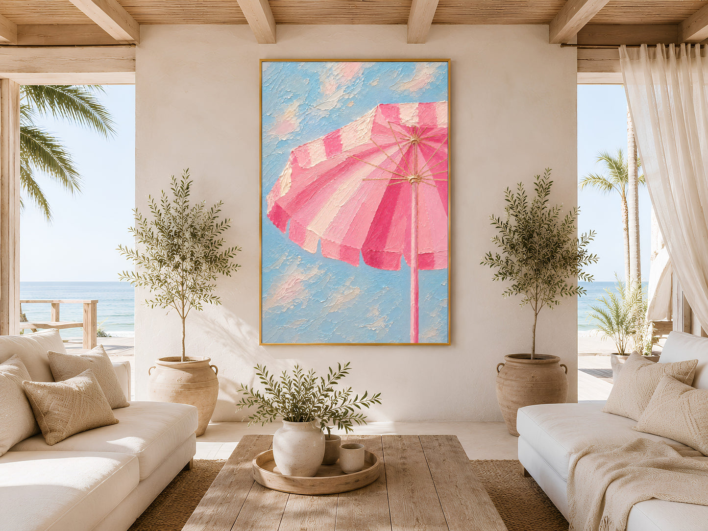 Framed pink beach umbrella wall art in a bright coastal living room with white sofa, wooden coffee table, olive tree and ocean view window
