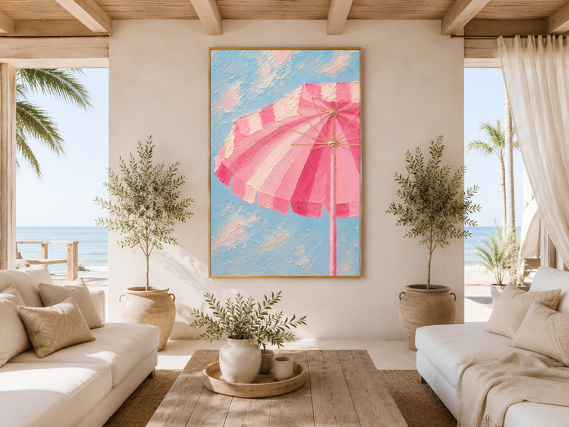 Framed pink beach umbrella wall art in a bright coastal living room with white sofa, wooden coffee table, olive tree and ocean view window
