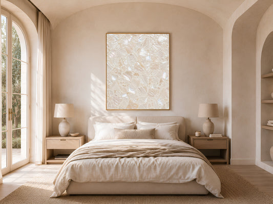 Warm coastal bedroom with an arched doorway, neutral linen bedding, and a framed terrazzo print hanging above the headboard.