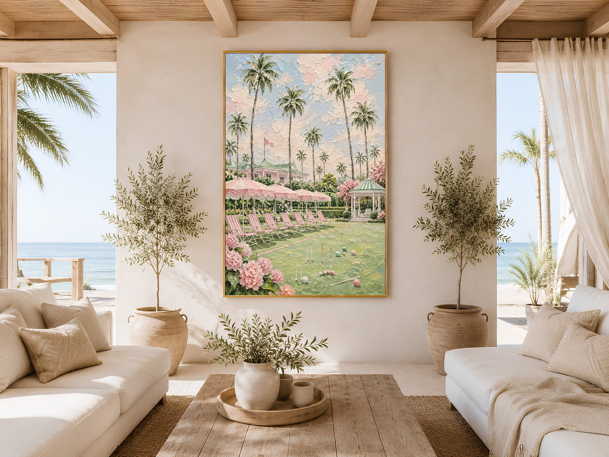 Gold-framed pink croquet lawn impasto print in a bright coastal living room with a cream sofa, potted olive tree, large windows, and warm natural light
