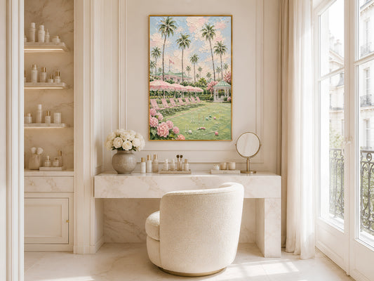 Gold-framed pink croquet lawn and palm tree impasto print in a bright bathroom beside a freestanding white bathtub with large windows and open shelving with flowers
