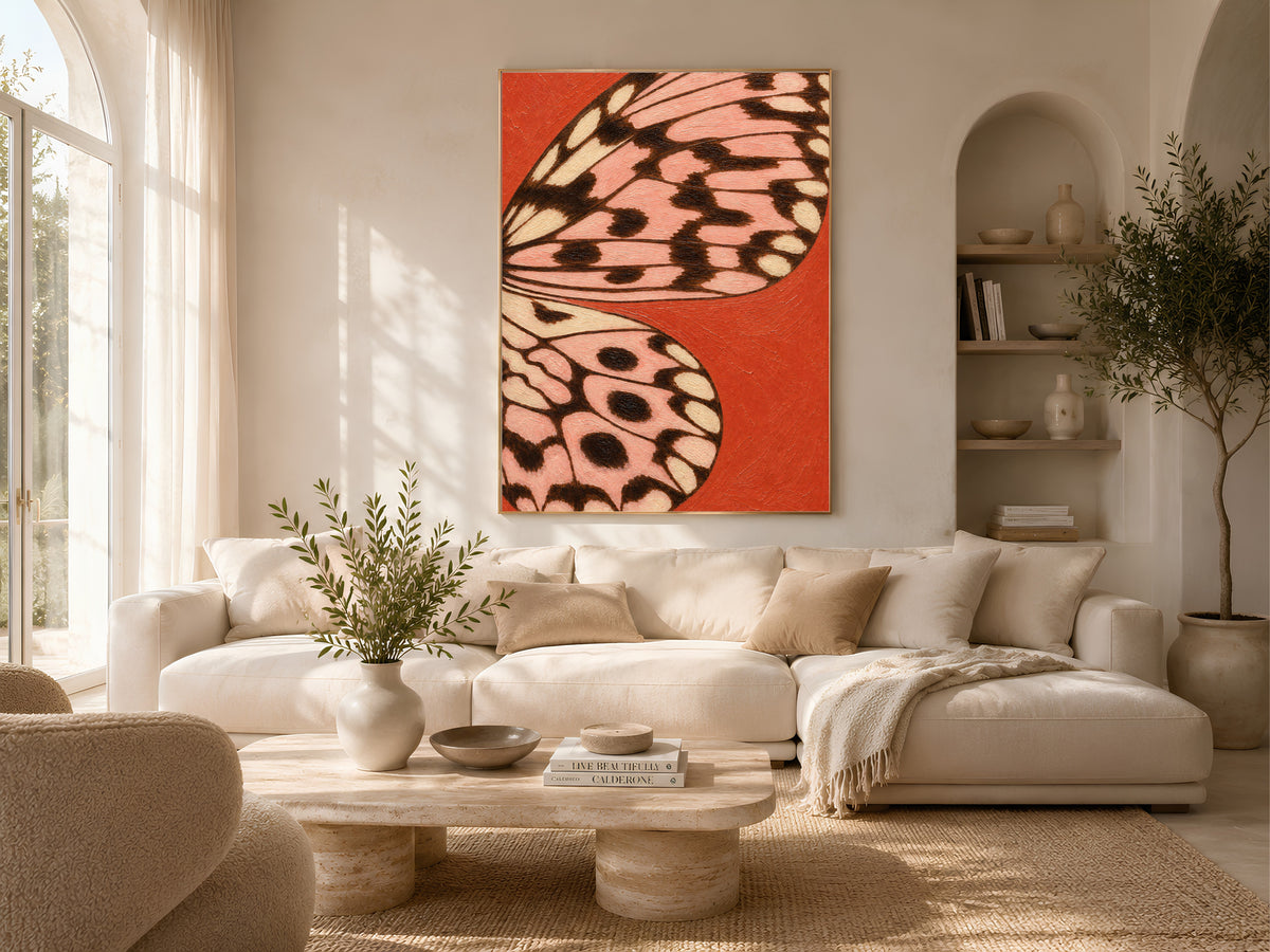 Tomato red and pink butterfly wing art framed on a wall above a sofa in a bright neutral living room