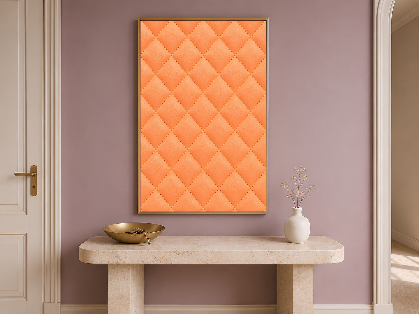 Quilted leather wall art in coral orange framed above a console table in a warm entryway