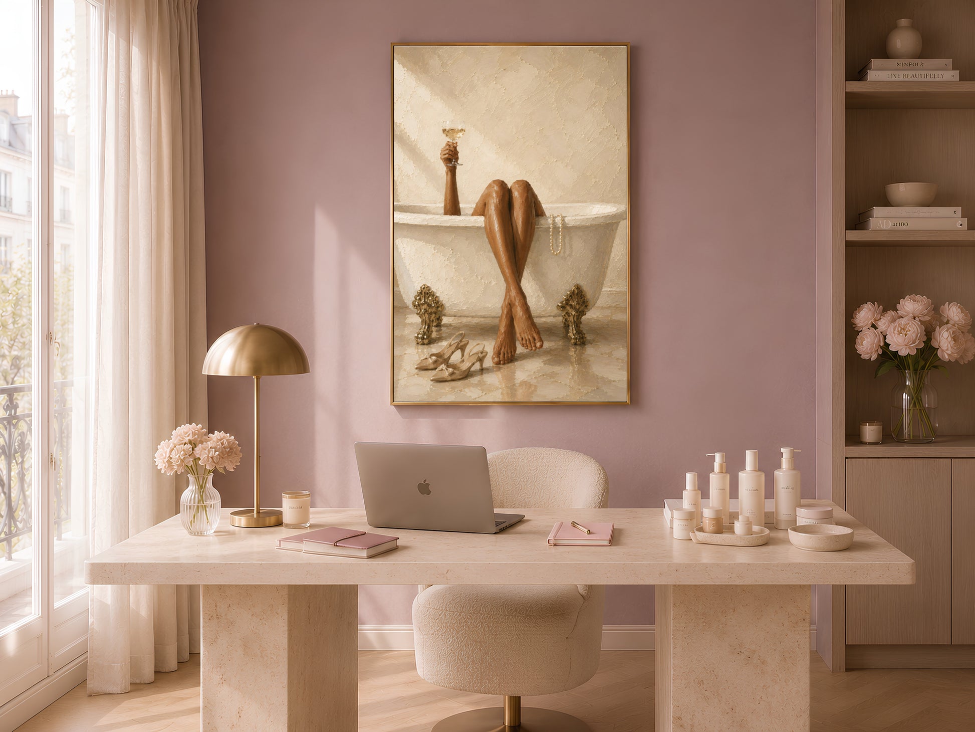 French interior wall art in a gold frame displayed on a dusty mauve wall above a travertine console table with a small lamp, candle, and bud vase