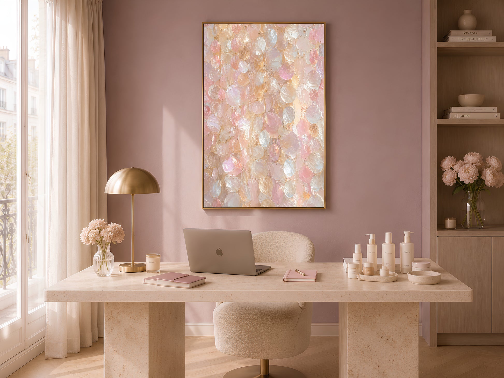 Capiz shell wall art print in a gold frame above a stone desk in a soft pink room with a brass lamp and white ceramic bottles
