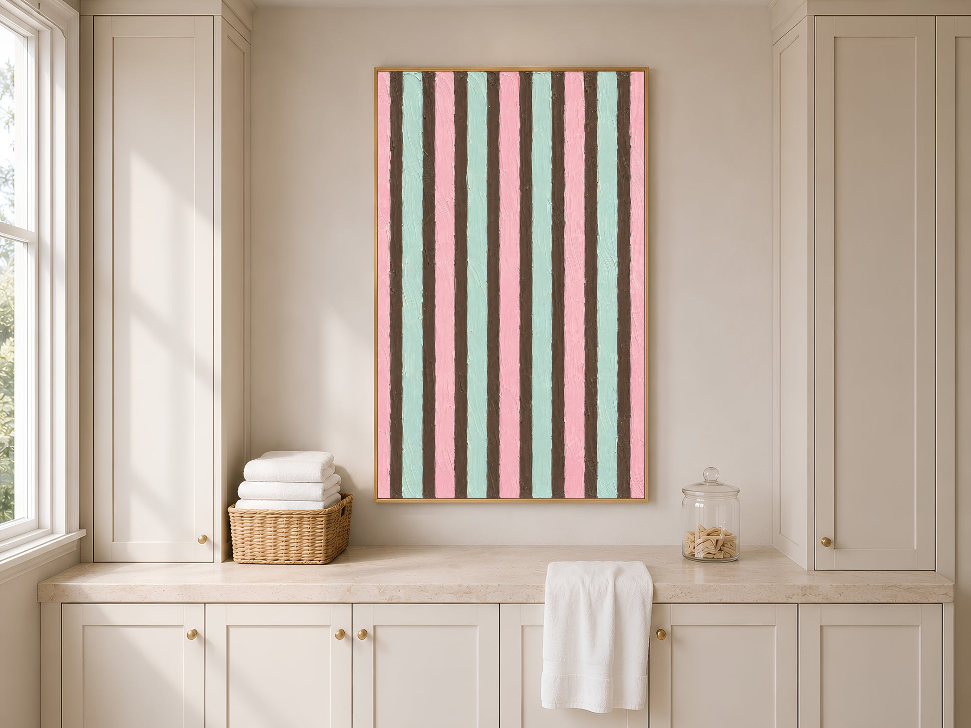 Pink mint stripe print in gold frame in bright utility room with white cabinetry and wicker basket
