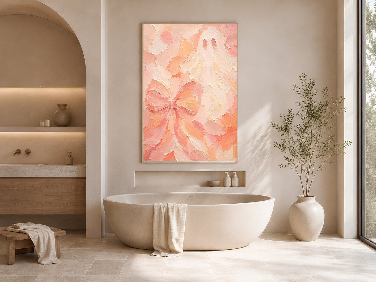 Pastel pink textured ghost and bow art print framed above a freestanding tub in a neutral bathroom