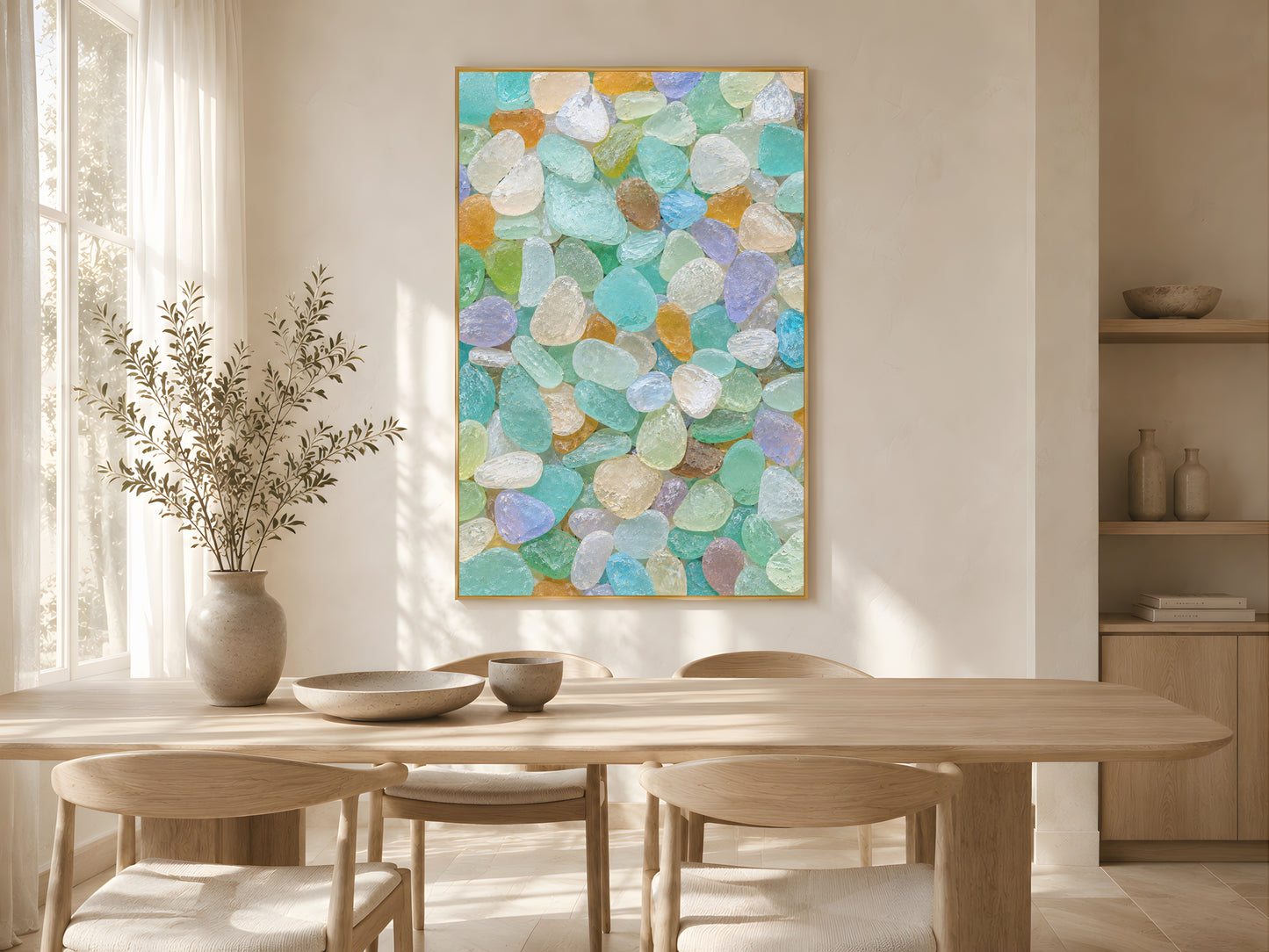 Colorful sea glass wall art in gold frame in bright coastal dining room with dried botanicals and oak table