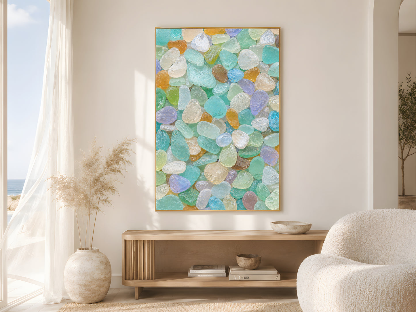Multicolor sea glass print in gold frame in bright coastal living room with cream armchair and pampas grass