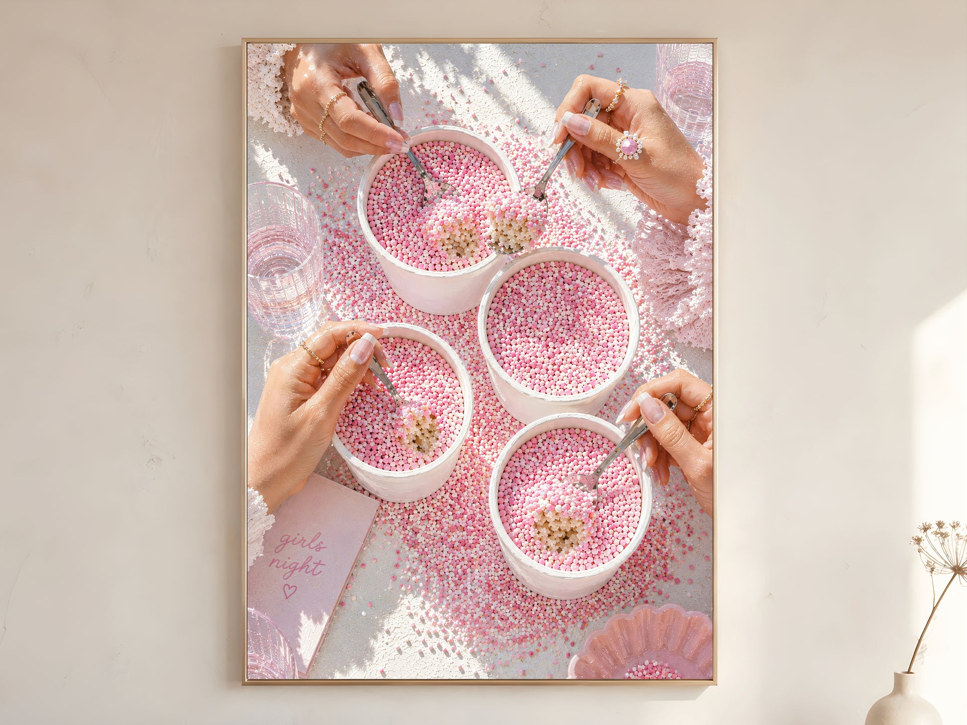 Pink coquette dot cake wall art print in a thin gold frame on a warm white wall showing four blush pink sprinkle dotcups held by manicured hands with diamond ring lace tablecloth and girls night card
