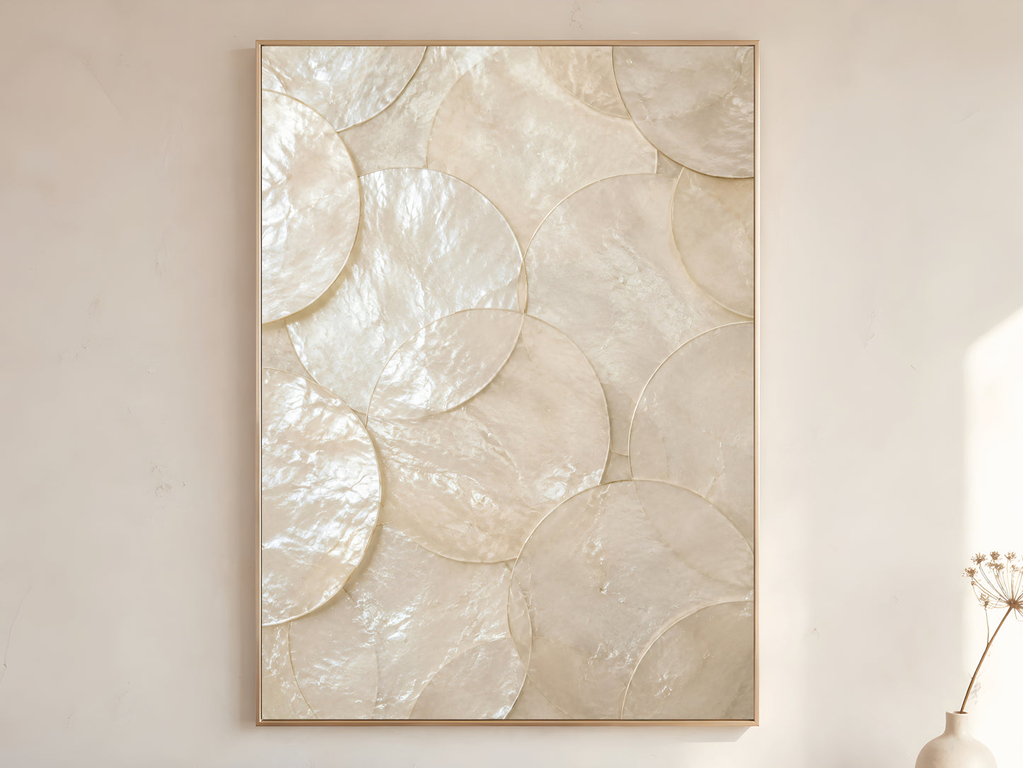 Large capiz shell wall art print in gold frame displayed on warm white living room wall showing oversized overlapping pearlescent shell discs with soft natural light

