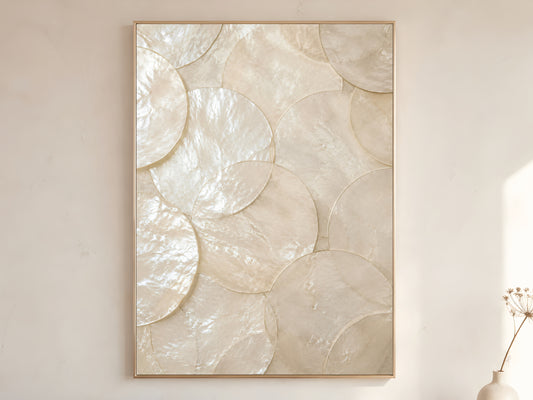 Large capiz shell wall art print in gold frame displayed on warm white living room wall showing oversized overlapping pearlescent shell discs with soft natural light

