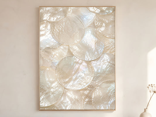 Mother of pearl iridescent shell wall art print in gold frame displayed on warm white living room wall showing large overlapping pearl white shell discs with rainbow shimmer
