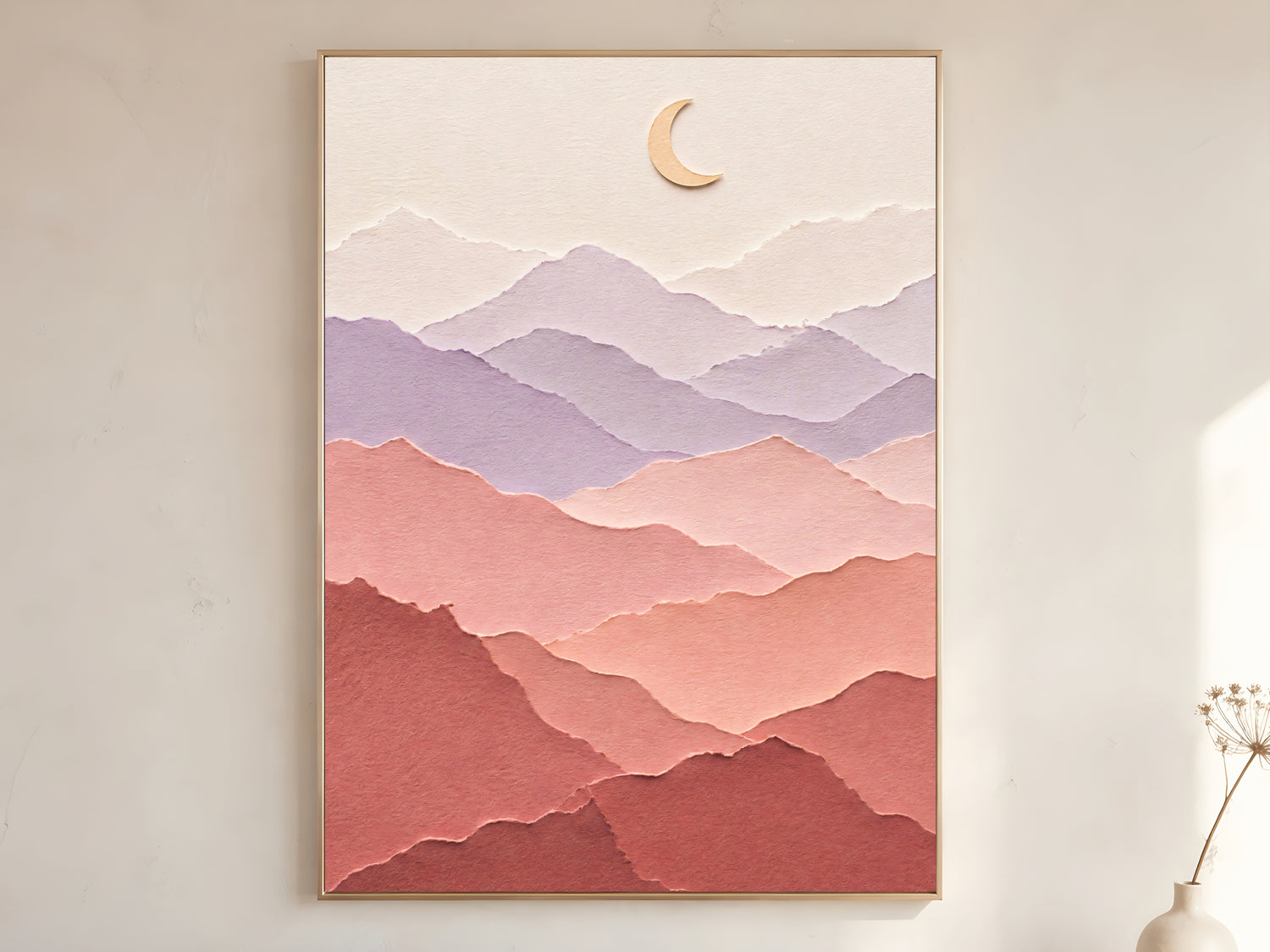 Pastel layered paper art mountain print with gold crescent moon in a thin gold frame on a warm white wall with a dried stem vase in a minimal living room
