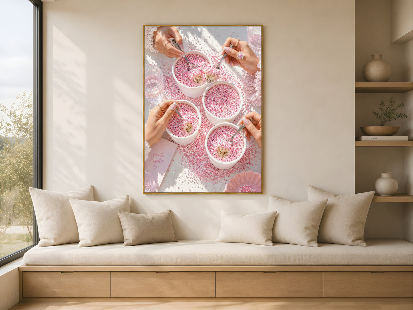 Pink coquette dot cake wall art print in a gold frame above a low linen bench in a bright minimal Scandinavian living room with warm afternoon light and dried stems
