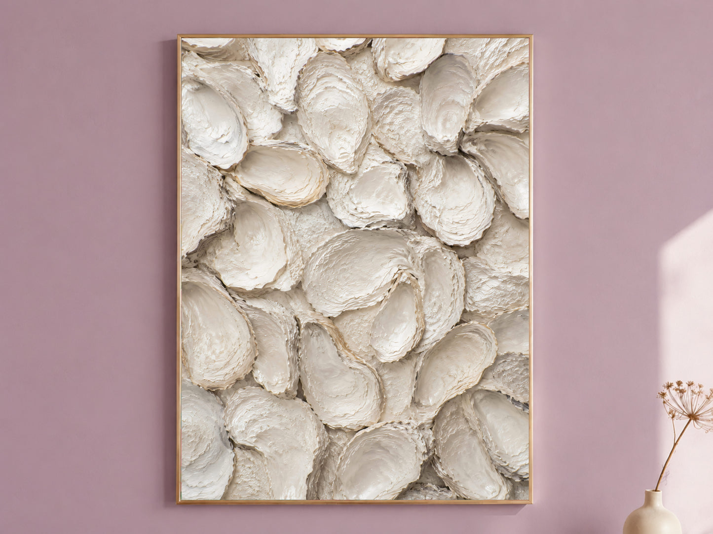Oyster shell wall art in a thin gold frame hanging on a dusty mauve wall, styled with a small dried flower vase.
