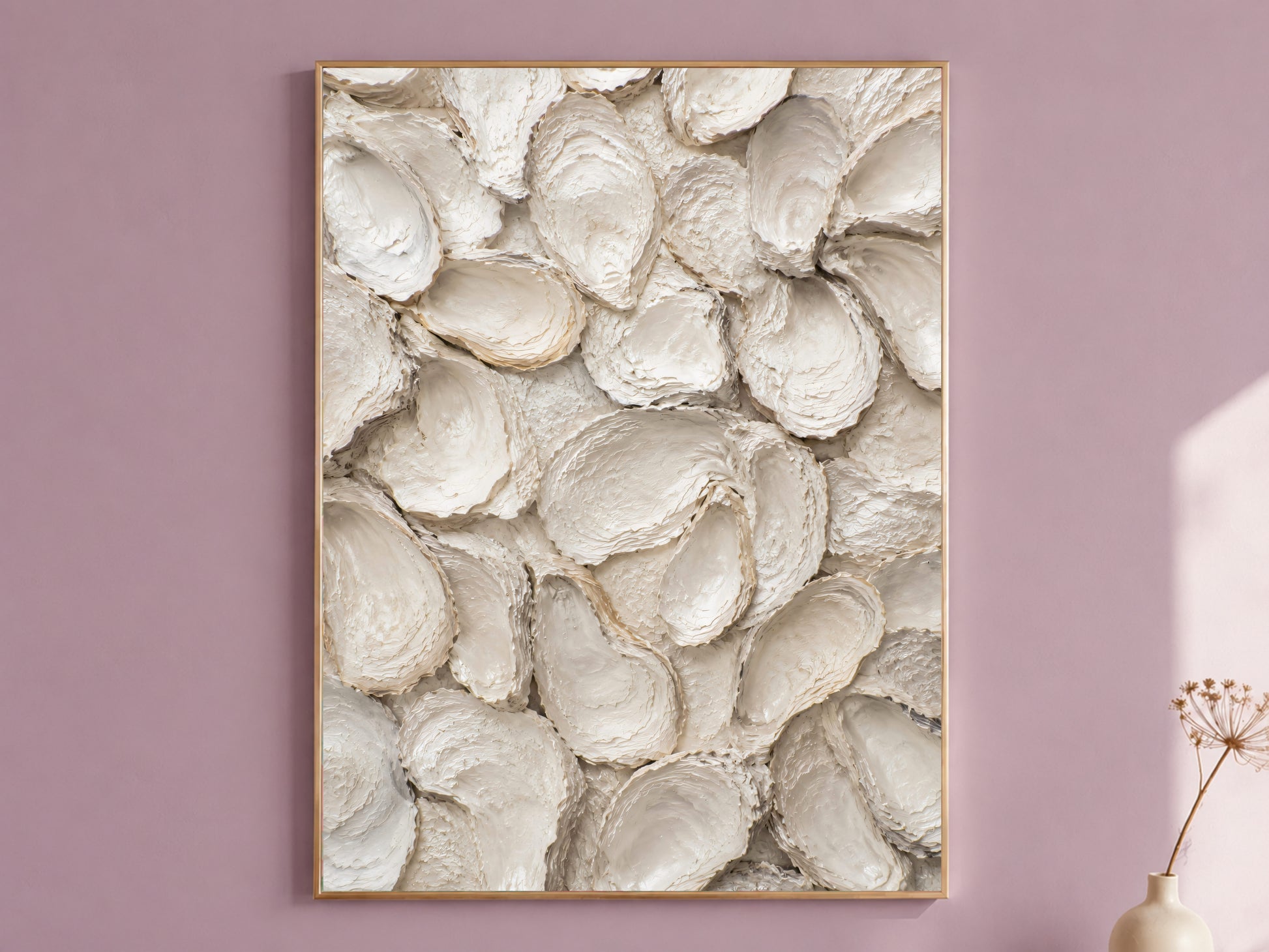 Oyster shell wall art in a thin gold frame hanging on a dusty mauve wall, styled with a small dried flower vase.