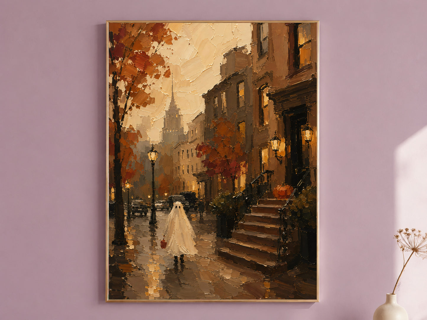 Brownstone Halloween art print in a thin gold frame on a mauve wall, ghost trick-or-treating past a stoop pumpkin, styled with a small vase of dried flowers