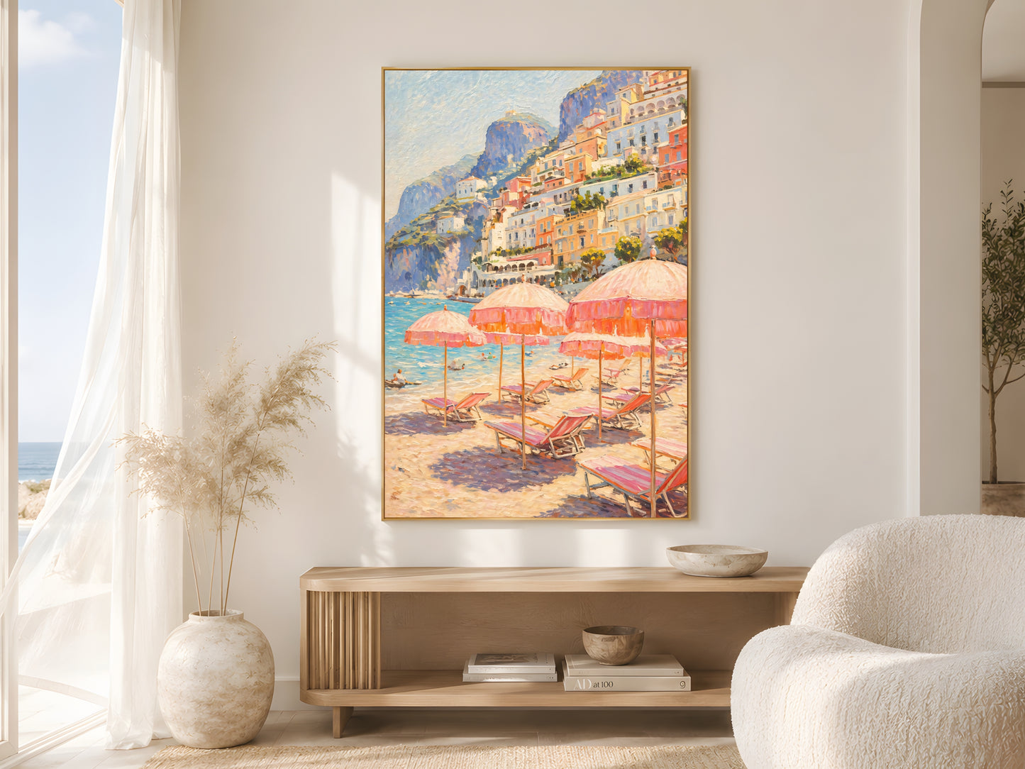 Positano beach club impasto wall art print in gold frame on warm white wall beside sheer curtains in bright coastal living room with cream bouclé armchair and dried pampas grass