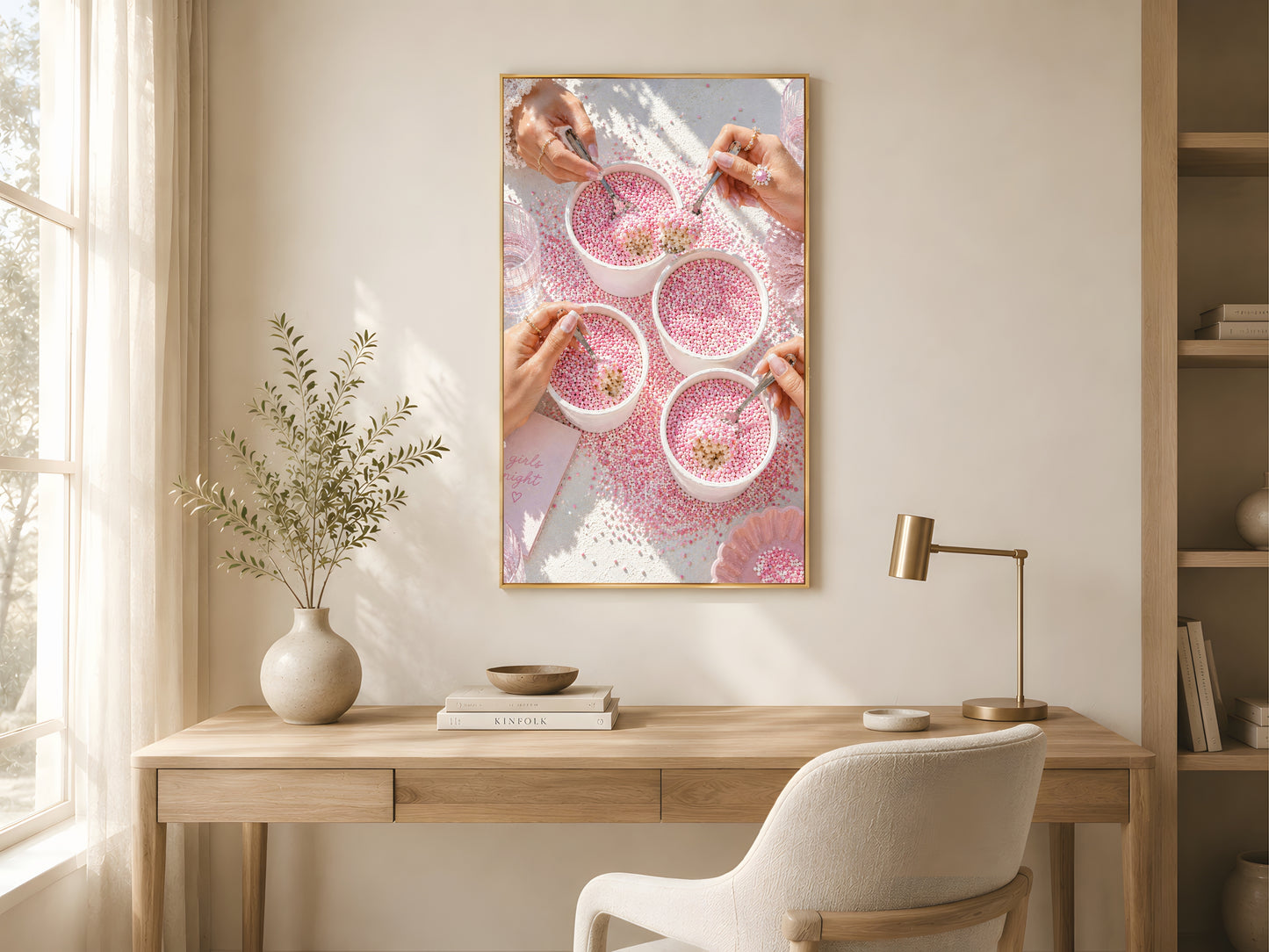 Pink coquette dot cake wall art print in a gold frame above a light oak desk in a bright minimal home office with white chair and warm natural light
