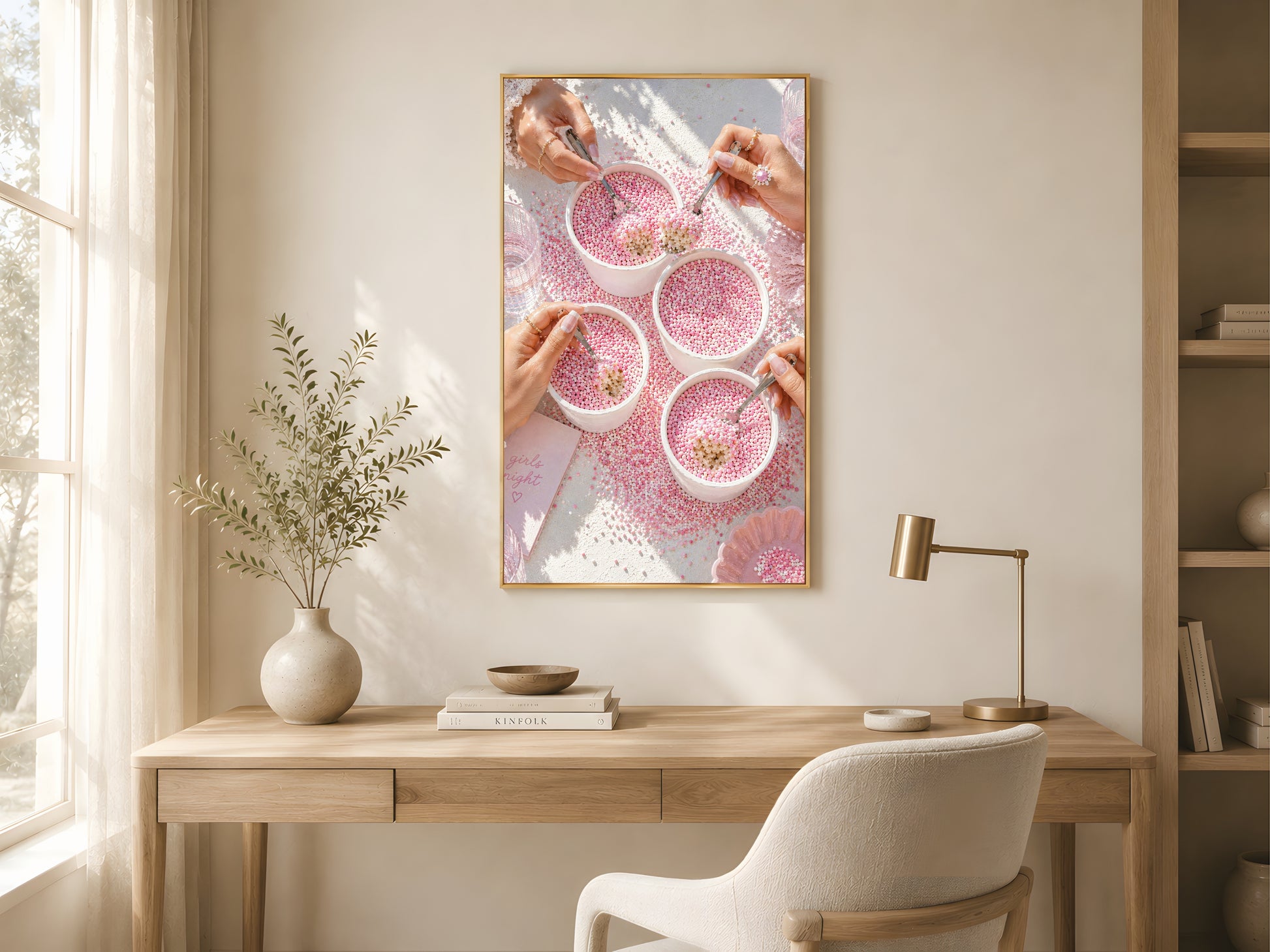 Pink coquette dot cake wall art print in a gold frame above a light oak desk in a bright minimal home office with white chair and warm natural light

