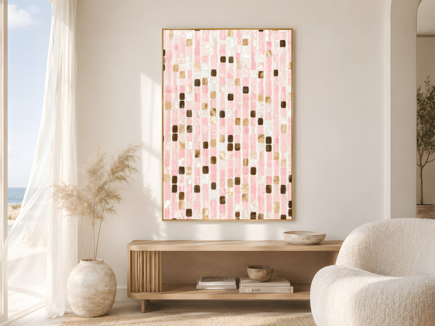 Pink mosaic tile print in gold frame beside sheer curtains in bright coastal living room with cream bouclé chair and dried pampas grass

