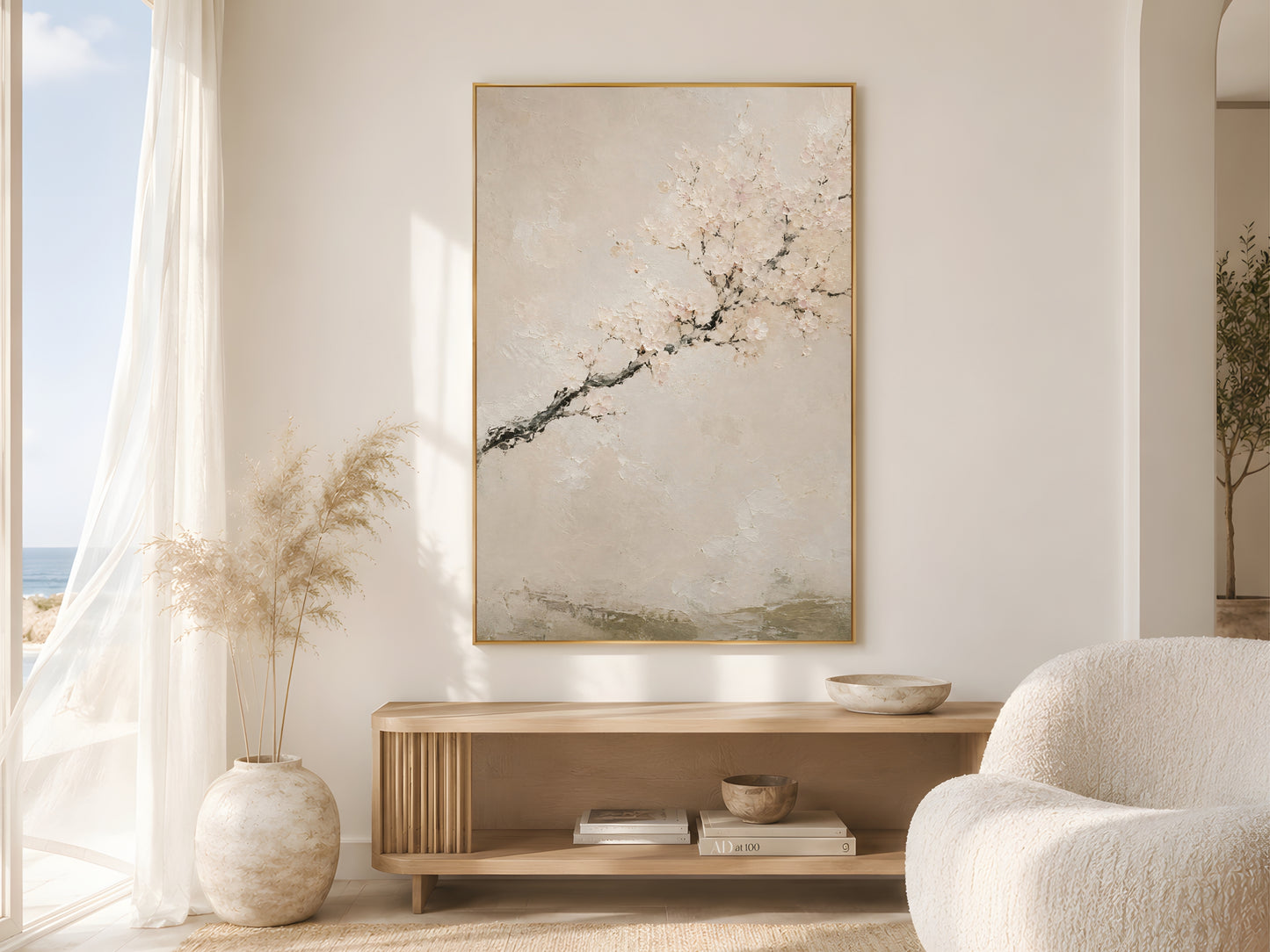 Japandi cherry blossom wall art print in a gold frame above a wooden console in a bright coastal living room with sheer curtains and pampas grass
