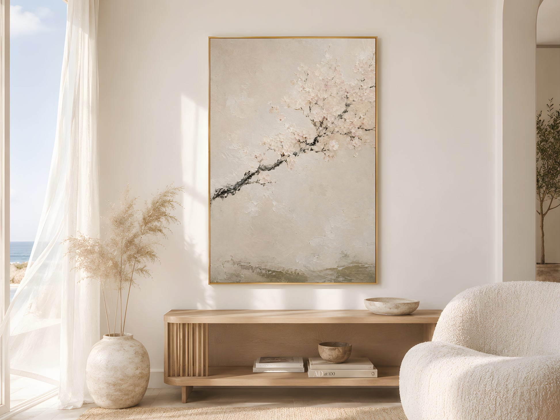 Japandi cherry blossom wall art print in a gold frame above a wooden console in a bright coastal living room with sheer curtains and pampas grass
