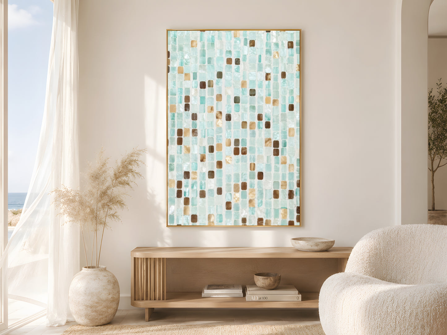 Teal mosaic coastal tile print in gold frame beside sheer curtains in bright coastal living room with cream bouclé chair and dried pampas grass

