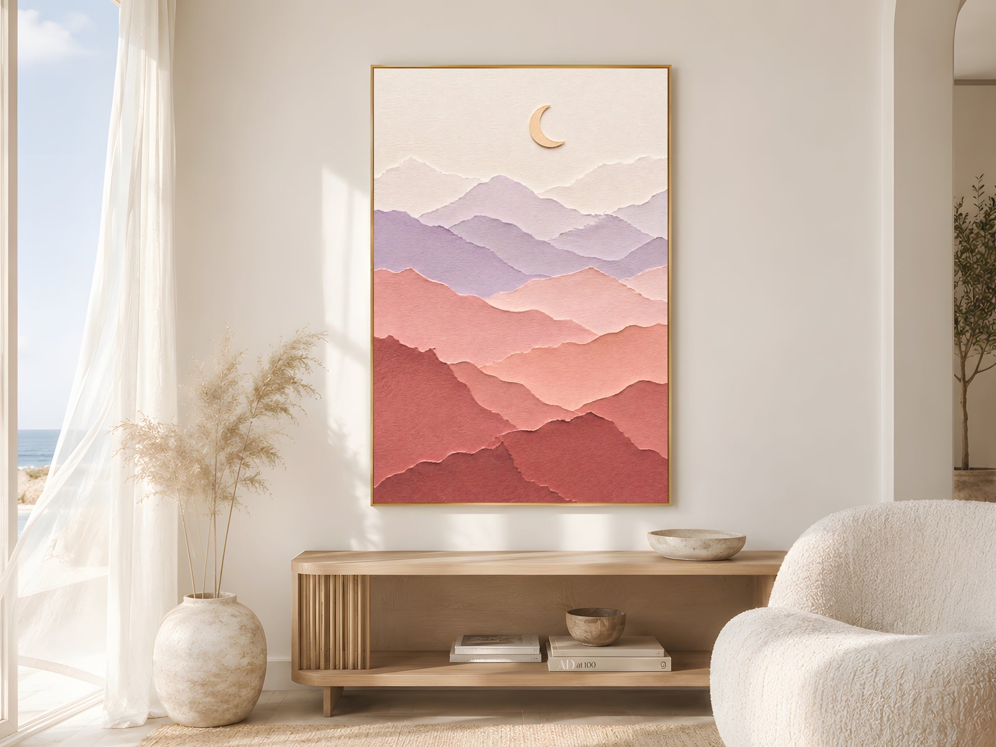 Pastel layered paper art mountain print in a gold frame beside sheer white curtains in a bright coastal living room with a round boucle chair
