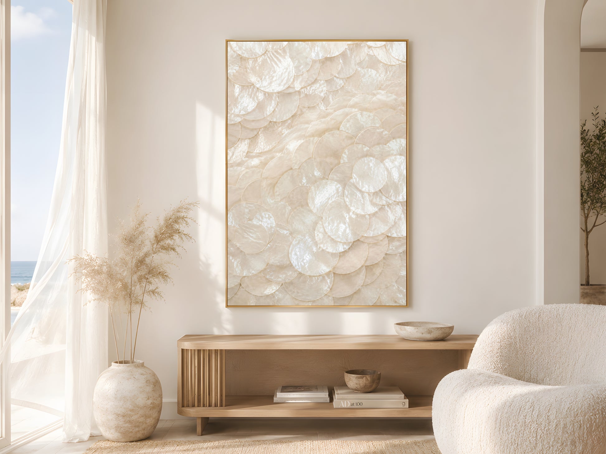 Capiz shell spiral swirl print in gold frame beside sheer curtains in bright coastal living room with cream bouclé chair and dried pampas grass
